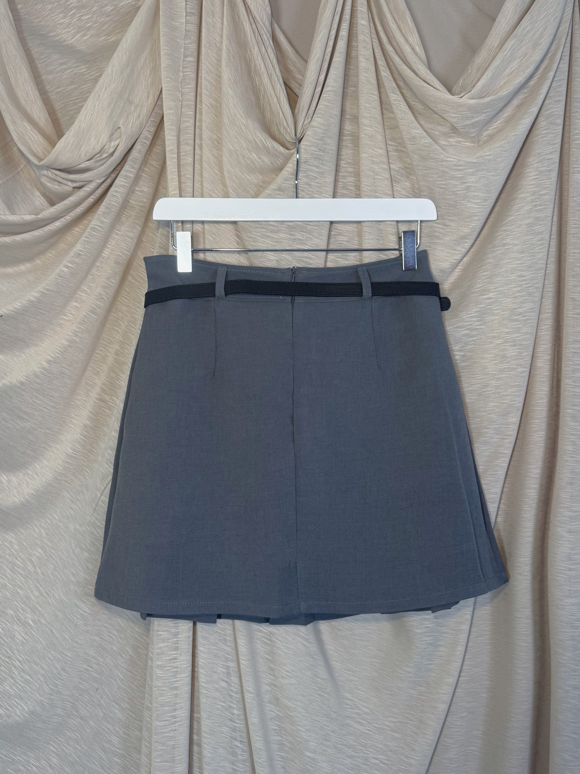 Jupe courte grise plissée en batavia avec une ceinture noire.