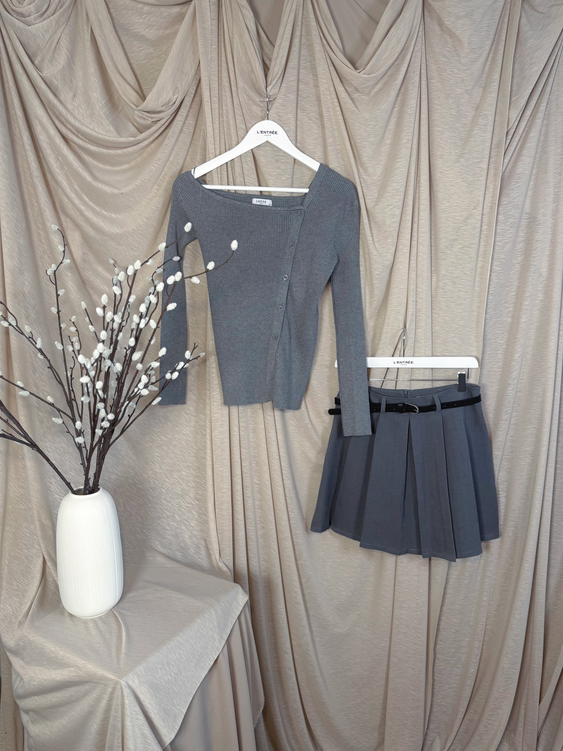 Jupe courte grise plissée en batavia avec une ceinture noire.