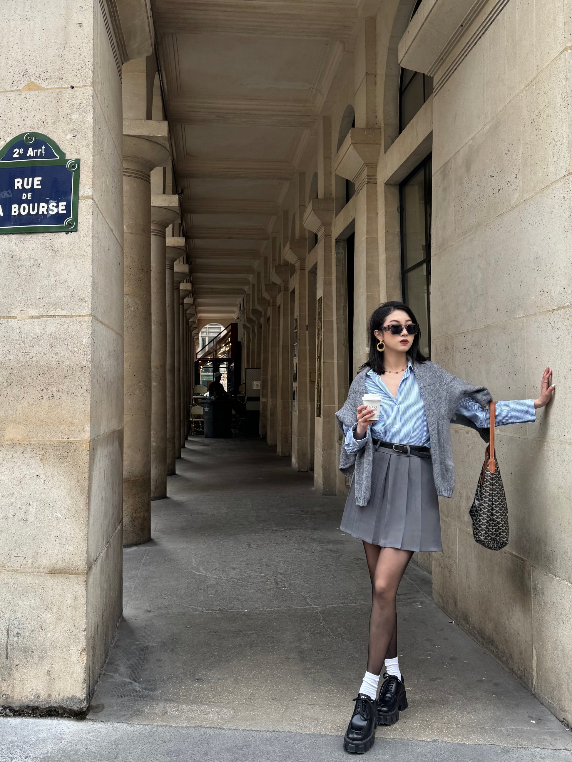 Jupe courte grise plissée en batavia avec une ceinture noire.