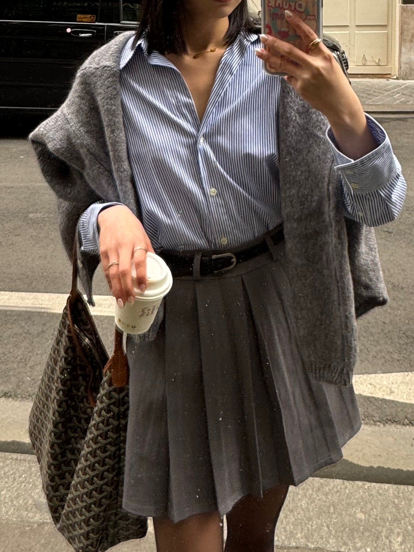 Jupe courte grise plissée en batavia avec une ceinture noire.