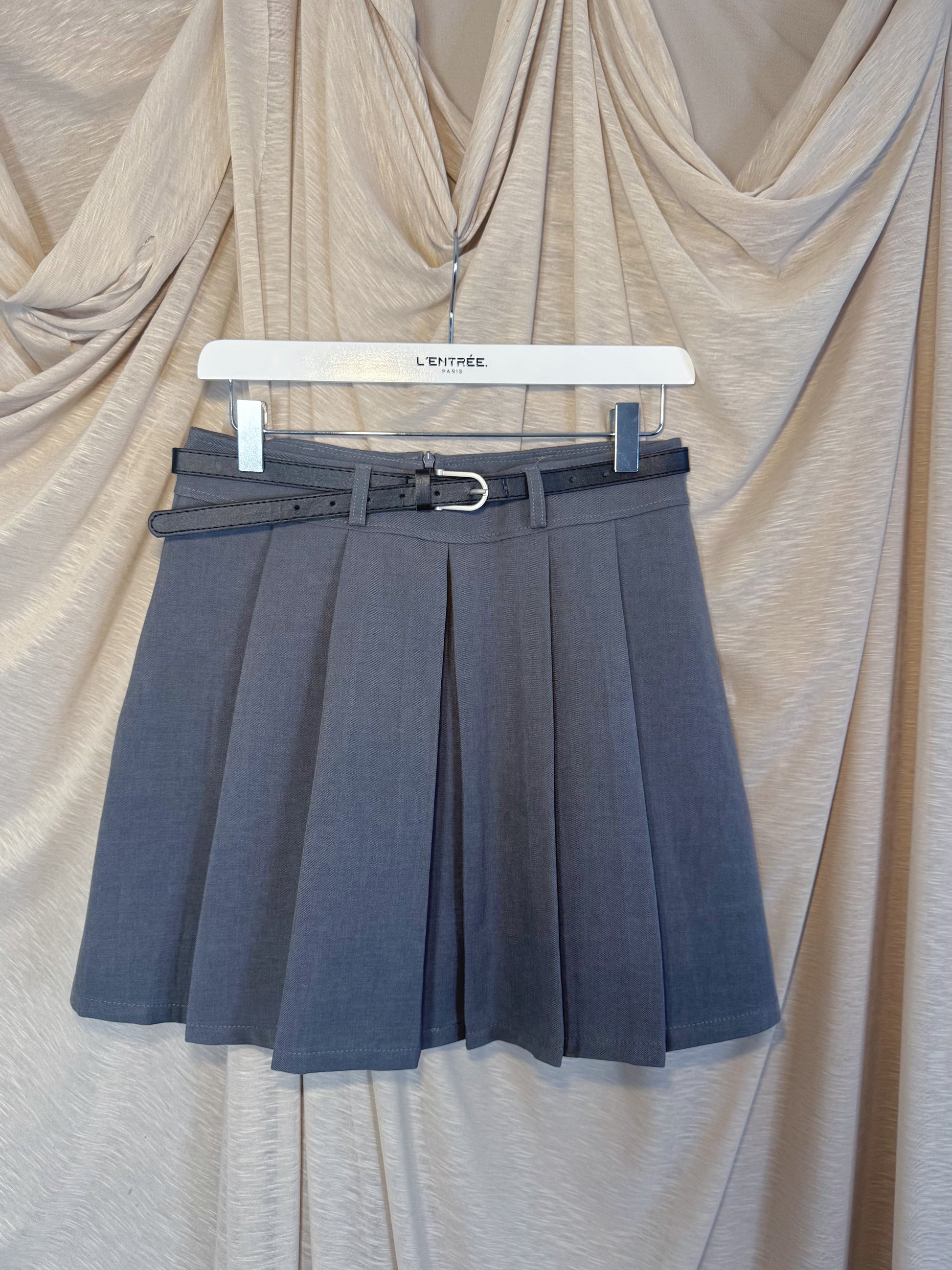 Jupe courte grise plissée en batavia avec une ceinture noire.