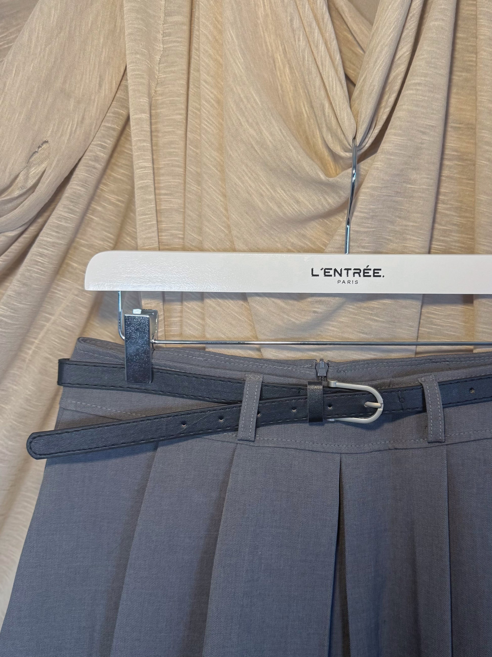 Jupe courte grise plissée en batavia avec une ceinture noire.